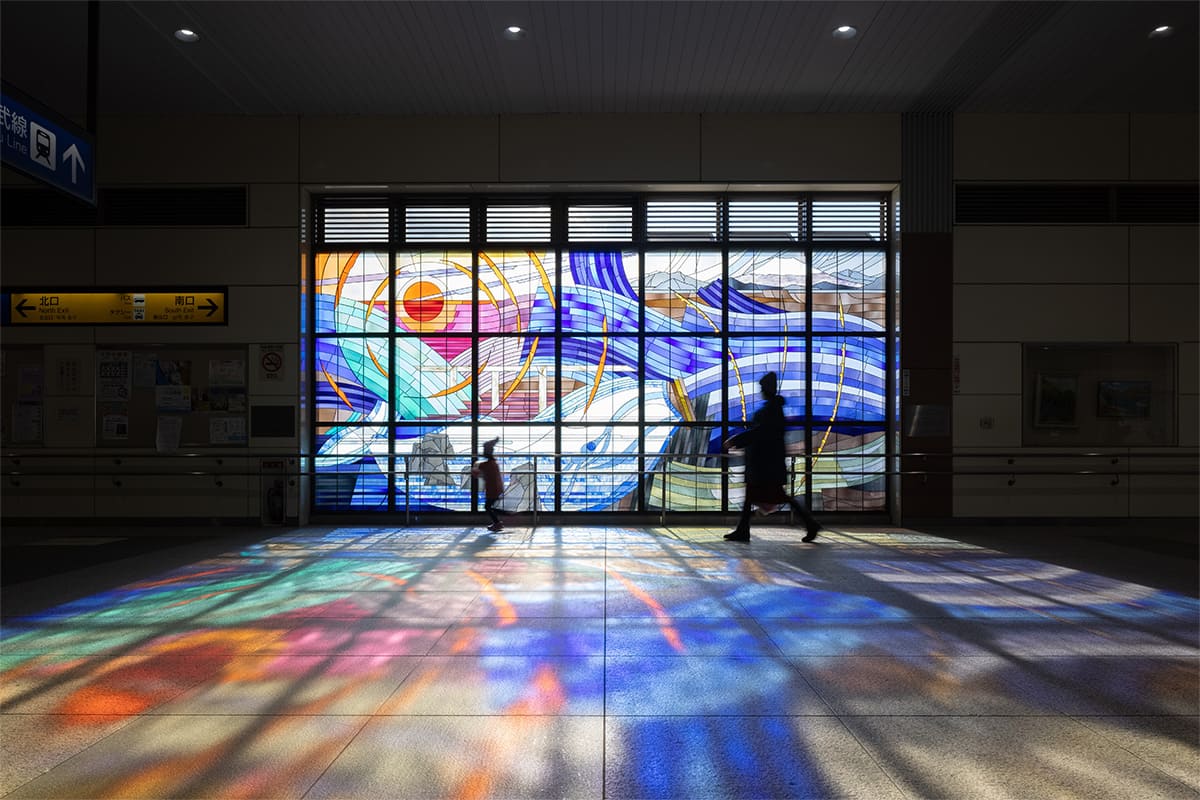 Full view of the Stained Glass artwork “Beautiful water flow, dream in the blowing wind : FUSSA / AKISHIMA” installed at Haijima Station